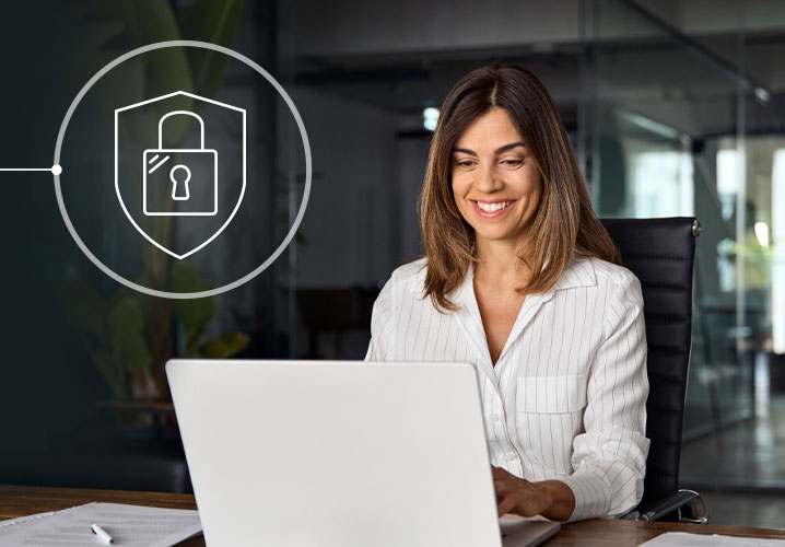 Eine lächelnde Frau arbeitet am Laptop, umgeben von Pflanzen, in einem modernen, hellen Büroraum.