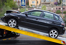 privater Versicherungsbereich: Schwarzes Auto wird auf einen Abschleppwagen geladen